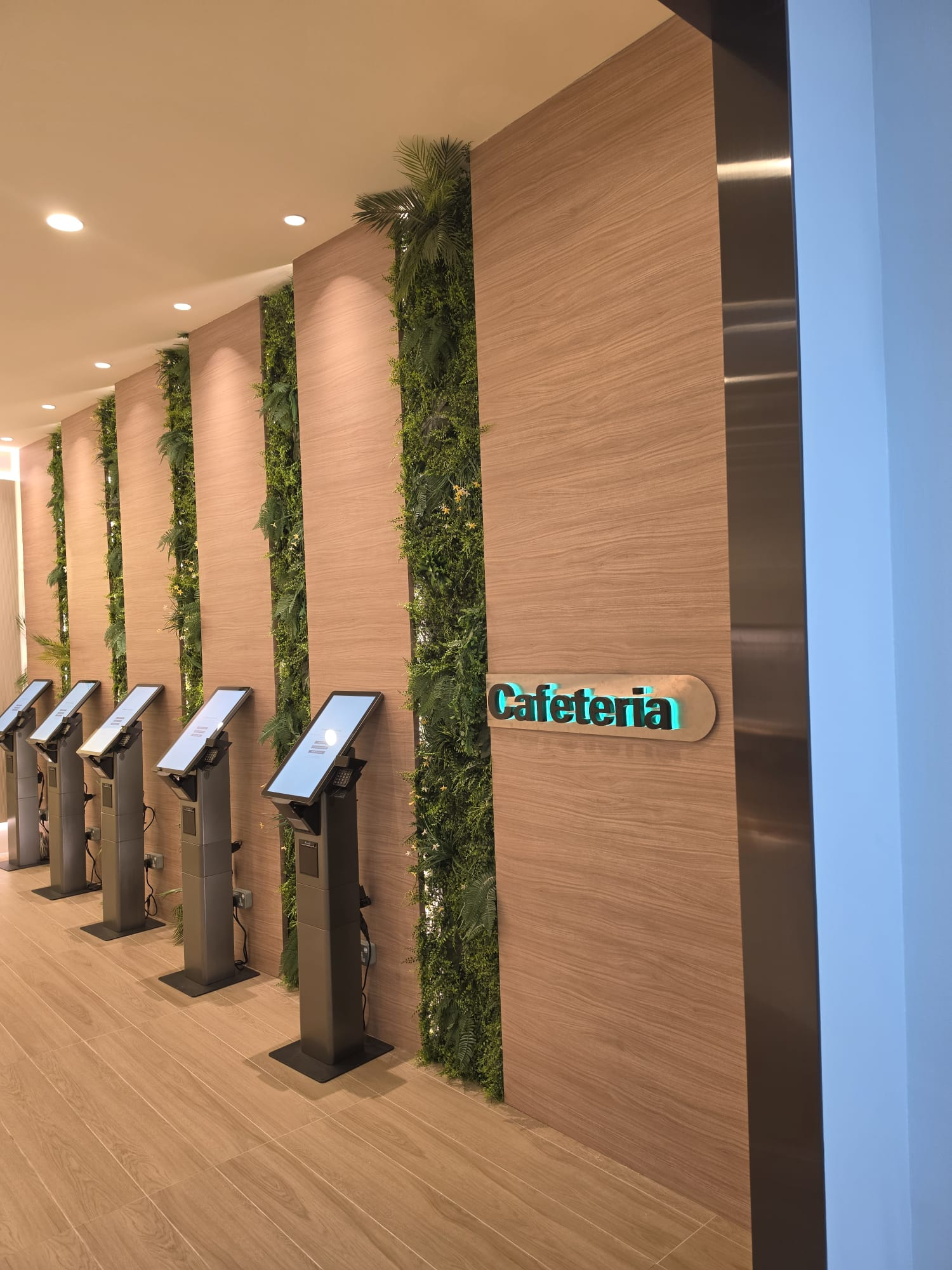 The Cafeteria interior with timber wall panels, vertical planting and self-service ordering kiosks.