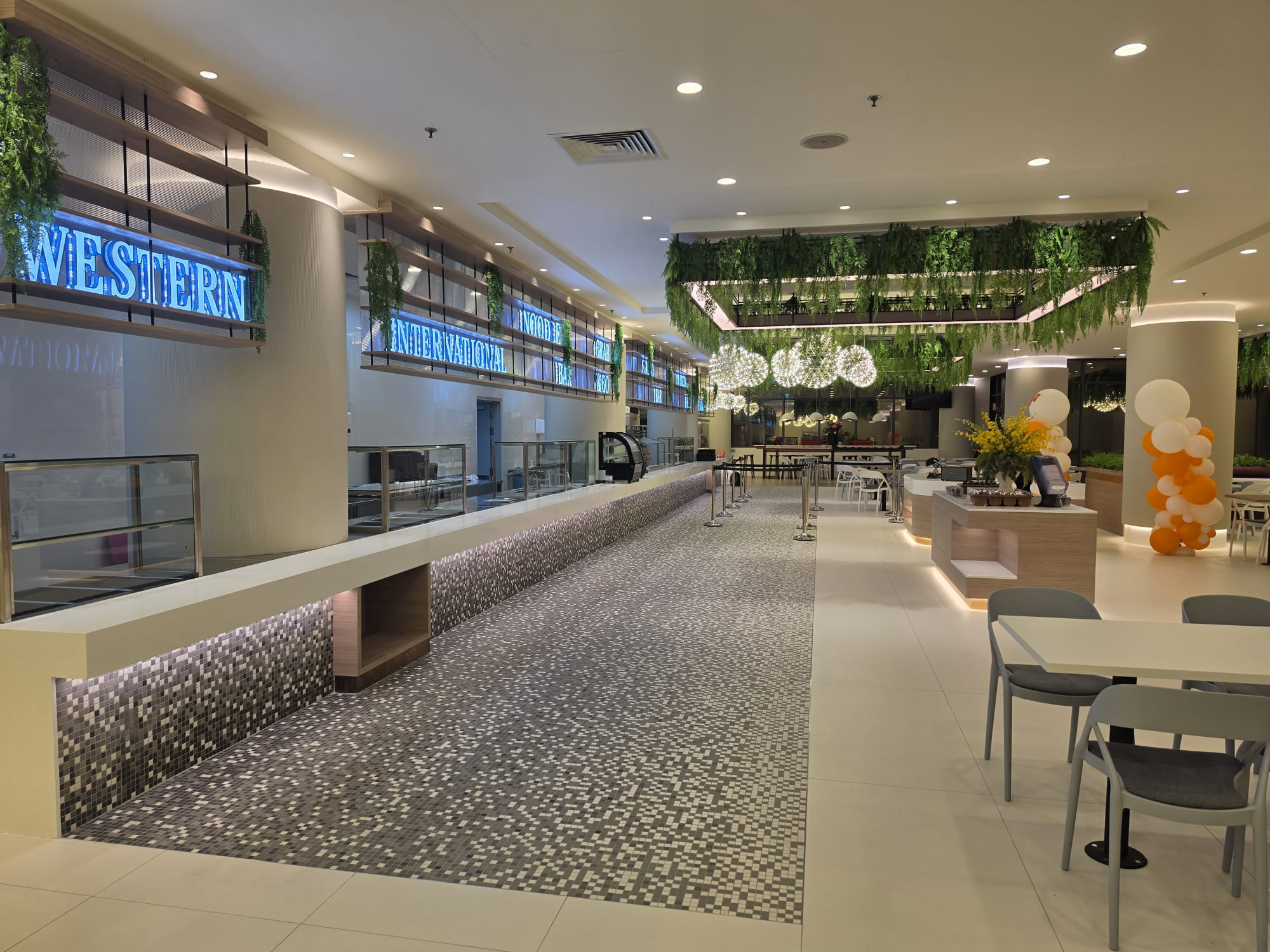 A food court with serving counters, mosaic flooring, pendant lights and hanging greenery.