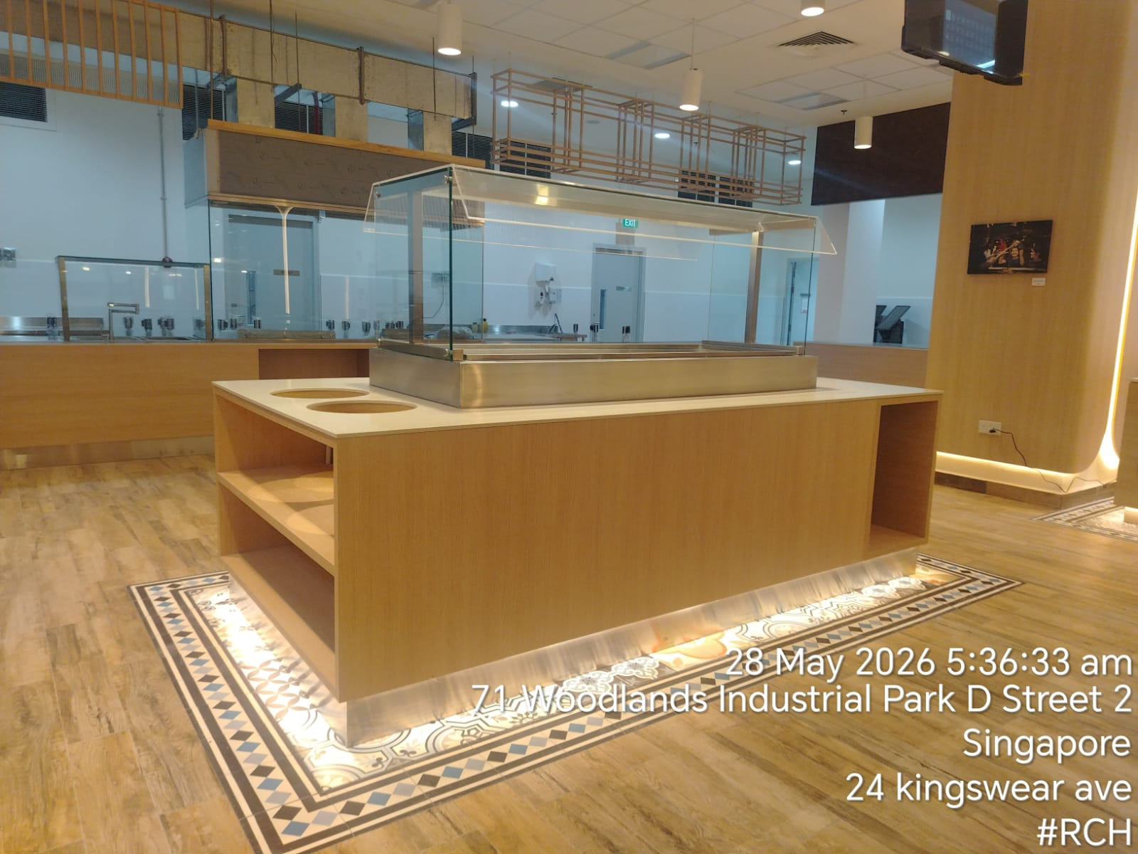 The Woodlands canteen interior with a timber-clad serving island, glass food display and patterned floor tiles.